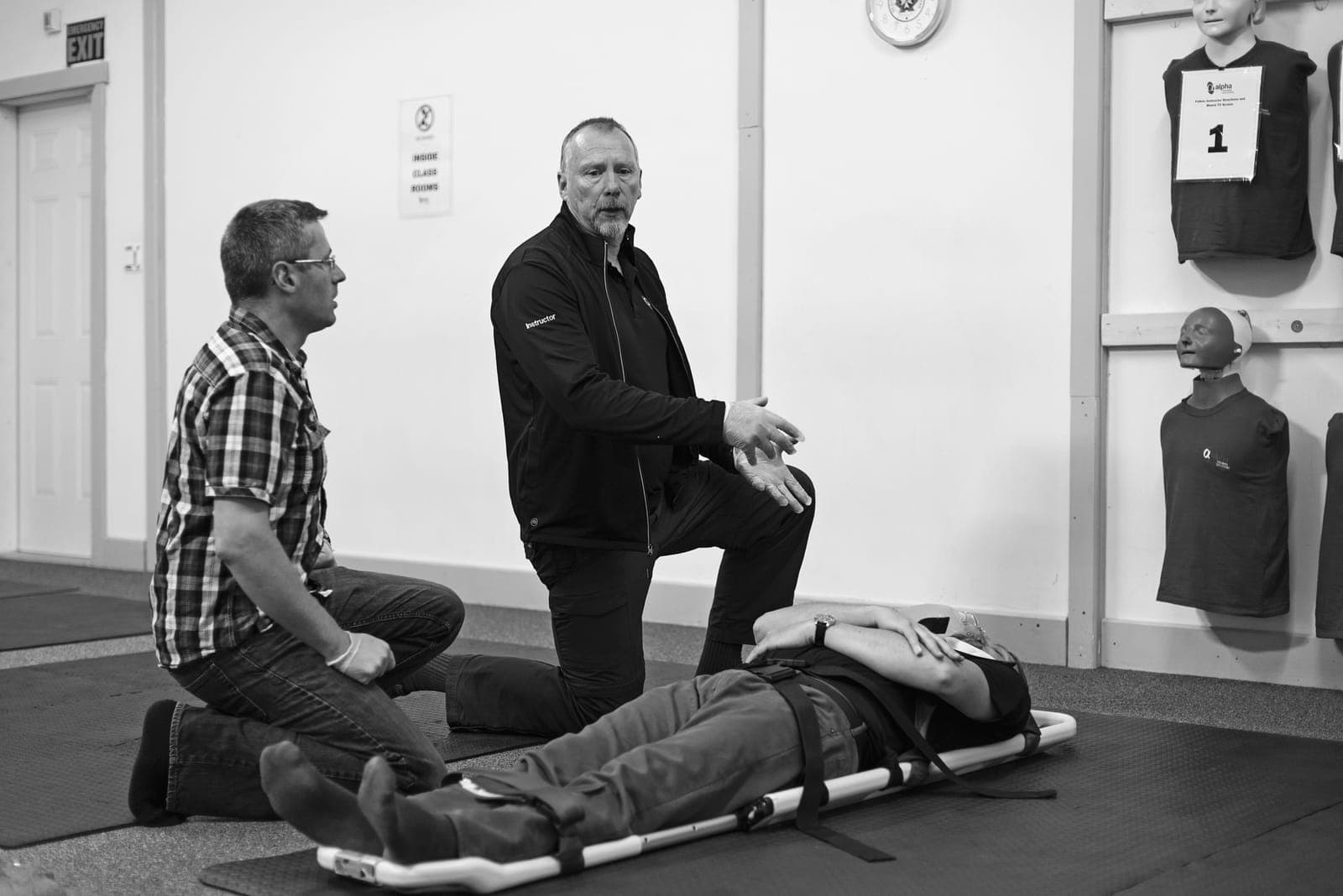 An instructor coaching two learners over a patient secured to a spine board on the training floor